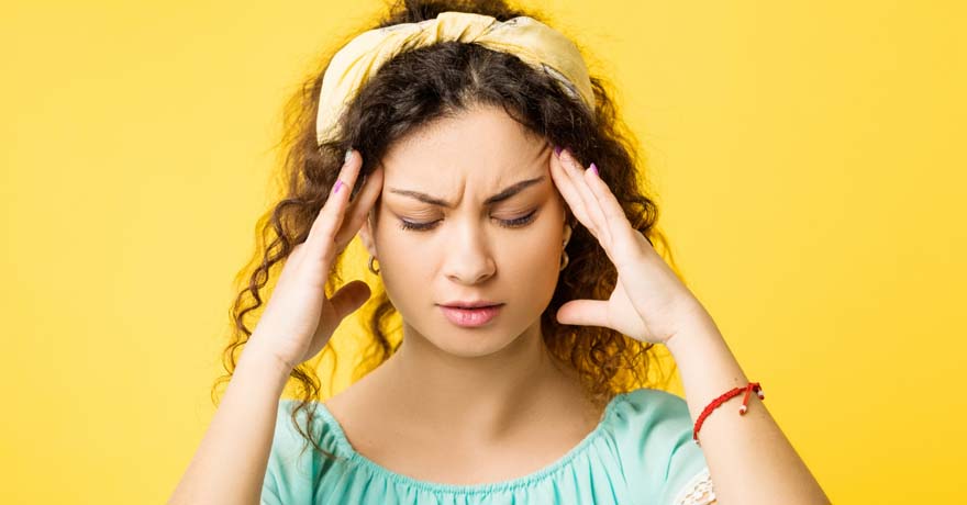 woman furrowing eyebrows in pain, hands on temples